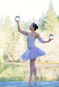 Ballerina in lavender tutu balances gracefully on pointe holding crystal balls outdoors. WA, USA