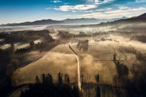 Drone recording in the morning mood with deep-horizontal early fog over brave mountain in Upper Bavaria in the back light