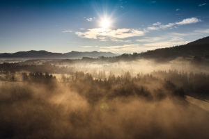 Drone recording in the morning mood with deep-horizontal early fog over brave mountain in Upper Bavaria in the back light