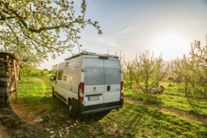 In spring, when the sun is shining and the sky is blue, a camper van stands idyllically on an orchard next to a wood pile. In front of it, a girl sits on a camping chair and reads a book. Breisach am Rhein, Kaiserstuhl, Baden-Wuerttemberg, Germany In spring, when the sun is shining and the sky is blue, a camper van stands idyllically on an orchard next to a wood pile. In front of it, a girl sits on a camping chair and reads a book. Breisach am Rhein, Kaiserstuhl, Baden-Wuerttemberg, Germany