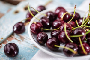 Cherries (Prunus) lie on a small porcelain plate on an old wooden table. Germany. Cherries (Prunus) lie on a small porcelain plate on an old wooden table. Germany.