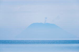 On the horizon above the sea, Stromboli emerges from the haze with its plume of smoke. Stromboli volcano, Sicily, Italy.