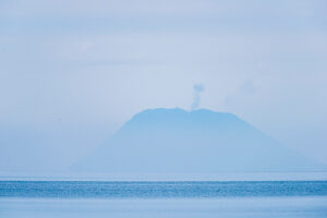 On the horizon above the sea, Stromboli emerges from the haze with its plume of smoke. Stromboli volcano, Sicily, Italy.