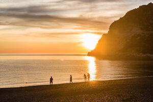 A small group of people walking on the beach at sunset at Cap Corse, Corsica, France. A small group of people walking on the beach at sunset at Cap Corse, Corsica, France.