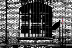 Closed industrial estate, 'No stopping' sign casting shadow on brick wall of old factory building, barred windows Closed industrial estate, 'No stopping' sign casting shadow on brick wall of old factory building, barred windows