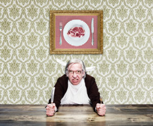 man wiht grey hair and glasses on the table, is holding knife and fork, photo with meat on the wall man wiht grey hair and glasses on the table, is holding knife and fork, photo with meat on the wall