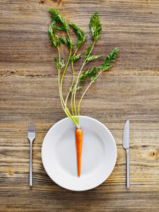 Carrot on plate, cutlery, knife and fork on old wooden table, from above
