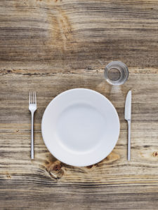 Empty plate, cutlery and glass on old wooden table, from above