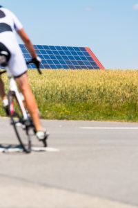 Road cyclist on country road, solar systems in the cornfield under a blue sky Road cyclist on country road, solar systems in the cornfield under a blue sky