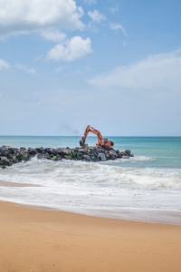 Excavator on a rock breakwater on the coast of Sri Lanka Excavator on a rock breakwater on the coast of Sri Lanka