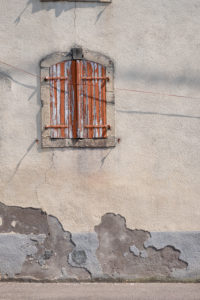 Windows in a weathered plaster facade with brown wooden shutters and peeling paint Windows in a weathered plaster facade with brown wooden shutters and peeling paint
