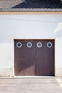brown wooden garage door with four round windows in a residential building with white plaster facade brown wooden garage door with four round windows in a residential building with white plaster facade