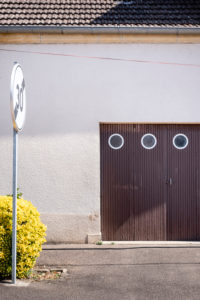 brown wooden garage door with three round windows in a residential building with white plaster facade at the end of a Tempo 30 zone brown wooden garage door with three round windows in a residential building with white plaster facade at the end of a Tempo 30 zone