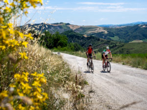 Zwei Rennradfahrer auf Tour im Apennin auf einer einsamen Bergstraße, Schotterstraße, Strade Bianchi in der Nähe von Predappio, Provinz Rimini in der Region Emilia-Romagna. Zwei Rennradfahrer auf Tour im Apennin auf einer einsamen Bergstraße, Schotterstraße, Strade Bianchi in der Nähe von Predappio, Provinz Rimini in der Region Emilia-Romagna.