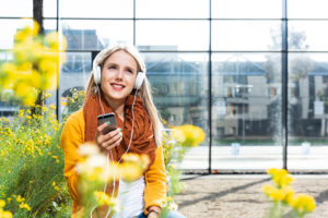 Young woman with Smartphone and earphones in front of office building, portrait Young woman with Smartphone and earphones in front of office building, portrait