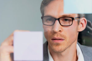 Young businessman reads Post-it in windowpane, portrait Young businessman reads Post-it in windowpane, portrait