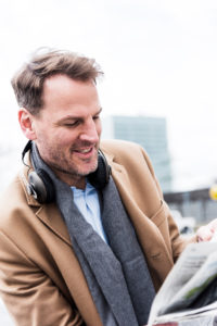 Businessman outside with earphones reads newspaper, portrait Businessman outside with earphones reads newspaper, portrait
