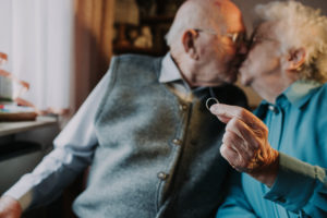 older couple, kiss, woman holds wedding ring into camera, 