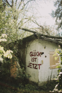 Old decayed garden house with the inscription 'Glück ist Jetzt' (Happiness is now) 