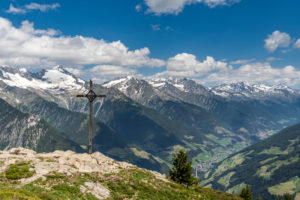 Sand in Taufers, Bolzano Province, South Tyrol, Italy. The summit cross on the Kleiner Nock in the Speikboden hiking area. In the background the Ahrntal with the Zillertal Alps Sand in Taufers, Bolzano Province, South Tyrol, Italy. The summit cross on the Kleiner Nock in the Speikboden hiking area. In the background the Ahrntal with the Zillertal Alps