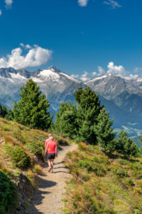 Sand in Taufers, Bolzano Province, South Tyrol, Italy. Hikers on the panorama trail in the Speikboden hiking area. In the background the Zillertal Alps with the Grosse Löffler Sand in Taufers, Bolzano Province, South Tyrol, Italy. Hikers on the panorama trail in the Speikboden hiking area. In the background the Zillertal Alps with the Grosse Löffler