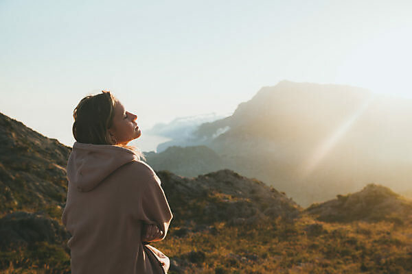 Pensive hiker using smart phone on mountain peak during sunrise at