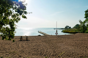 Sandstrand mit Bank, Steg und Rettungsring, eingerahmt von Grün Sandstrand mit Bank, Steg und Rettungsring, eingerahmt von Grün