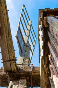 Flügelblatt einer Bockwindmühle vor blauem Himmel eingerahmt vom Mühlenbauwerk Flügelblatt einer Bockwindmühle vor blauem Himmel eingerahmt vom Mühlenbauwerk
