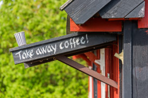 Kaffeebecher steht auf Vordach mit Take away coffee Schriftzug, Holzhaus im Anschnitt Kaffeebecher steht auf Vordach mit Take away coffee Schriftzug, Holzhaus im Anschnitt