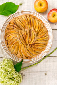 Apfelkuchen in runder Form gebacken und dekorativ mit Apfelspalten belegt, dekoriert mit zwei Äpfeln und einer weißen Hortensienblüte Apfelkuchen in runder Form gebacken und dekorativ mit Apfelspalten belegt, dekoriert mit zwei Äpfeln und einer weißen Hortensienblüte