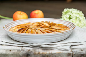 Apfelkuchen in runder Form gebacken und dekorativ mit Apfelspalten belegt, dekoriert mit zwei Äpfeln und einer weißen Hortensienblüte Apfelkuchen in runder Form gebacken und dekorativ mit Apfelspalten belegt, dekoriert mit zwei Äpfeln und einer weißen Hortensienblüte