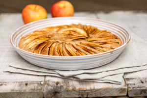 Apfelkuchen in runder Form gebacken und dekorativ mit Apfelspalten belegt, dekoriert mit zwei Äpfeln Apfelkuchen in runder Form gebacken und dekorativ mit Apfelspalten belegt, dekoriert mit zwei Äpfeln