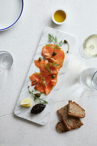 Smoked salmon slices with caper apples on a marble serving platter