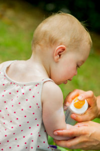 Parent spraying sunscreen on baby's arm