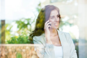 Businesswoman looking out of window from office while using cell phone