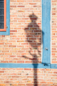 Europe, Germany, Lower Saxony, Otterndorf. In the morning sun, the shadow of an old street lamp falls onto the bare red brick wall of the teahouse. Europe, Germany, Lower Saxony, Otterndorf. In the morning sun, the shadow of an old street lamp falls onto the bare red brick wall of the teahouse.