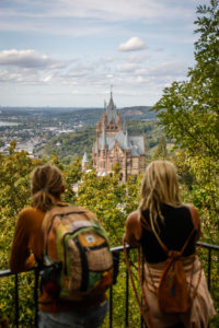 Koenigswinter, North Rhine-Westphalia, Germany - Drachenburg Castle on the Drachenfels, attraction and excursion destination in the Siebengebirge on the Rhine, young tourists with dreadlocks at the viewpoint in front of the northern Rhine Valley. Koenigswinter, North Rhine-Westphalia, Germany - Drachenburg Castle on the Drachenfels, attraction and excursion destination in the Siebengebirge on the Rhine, young tourists with dreadlocks at the viewpoint in front of the northern Rhine Valley.