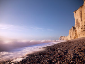The cliffs of Étretat glow in the evening sun. View from the beach to the Porte D'Amont rock gate The cliffs of Étretat glow in the evening sun. View from the beach to the Porte D'Amont rock gate