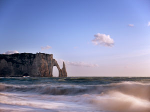 The Porte D'Aval and Aiguille rock gates at Étretat. The surf and cliffs are illuminated by the evening sun The Porte D'Aval and Aiguille rock gates at Étretat. The surf and cliffs are illuminated by the evening sun