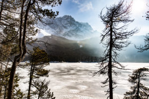 The frozen Eibsee in front of the Zugspitze in Germany. View through the trees. The frozen Eibsee in front of the Zugspitze in Germany. View through the trees.
