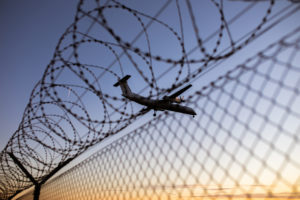 Airplane in the blue sky over a barbed wire fence Airplane in the blue sky over a barbed wire fence