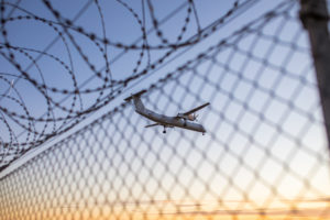 Airplane in the blue sky over a barbed wire fence Airplane in the blue sky over a barbed wire fence