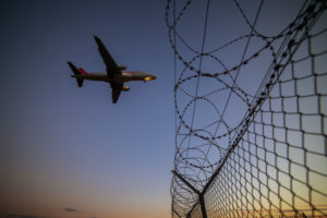 Airplane in the blue sky over a barbed wire fence Airplane in the blue sky over a barbed wire fence