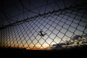 Airplane in the blue sky over a barbed wire fence Airplane in the blue sky over a barbed wire fence