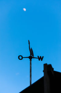 The blurred moon in the blue sky, in the foreground a weathercock The blurred moon in the blue sky, in the foreground a weathercock