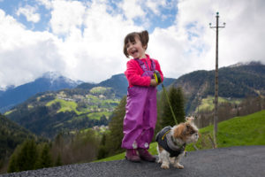 4-6 jähriges Mädchen mit mit Regenhose und Hund steht lachend am Straßenrand 4-6 jähriges Mädchen mit mit Regenhose und Hund steht lachend am Straßenrand
