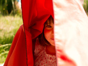 4-6 jähriges Mädchen unter rotem Badetuch auf Wiese 4-6 jähriges Mädchen unter rotem Badetuch auf Wiese