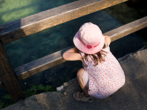 4-6 jähriges Mädchen mit Rosa Hut am Rand von einem See, blickt ins Wasser 4-6 jähriges Mädchen mit Rosa Hut am Rand von einem See, blickt ins Wasser