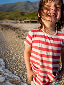 4-6 jähriges Mädchen in gestreiftem T-Shirt, lachend am Strand 4-6 jähriges Mädchen in gestreiftem T-Shirt, lachend am Strand
