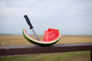 Messer steckt in aufgeschnittenem Melonenstück auf einem Holzbalken Messer steckt in aufgeschnittenem Melonenstück auf einem Holzbalken